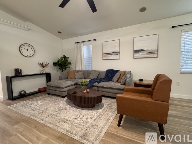 A living room with a grey sofa, a brown armchair, a coffee table, and a large clock on the wall.