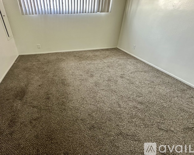 A room with a carpeted floor and a window with blinds.