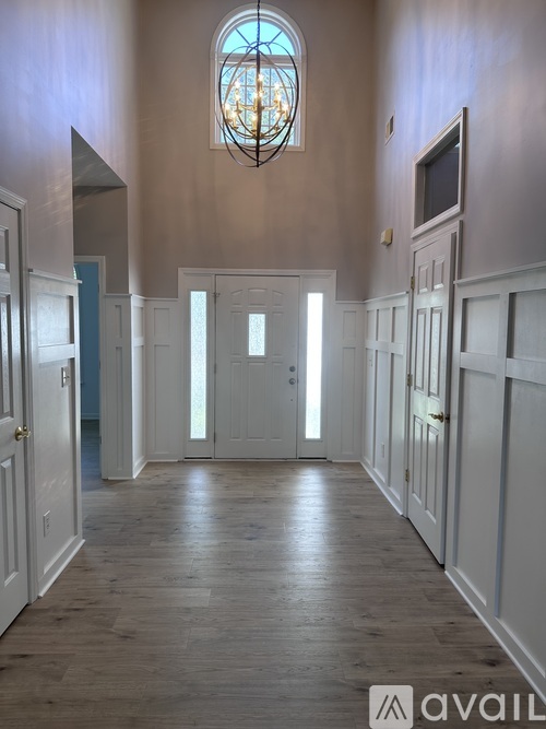 A hallway with a wooden floor and white walls leading to a door.