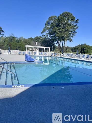 A pool with a blue lounge chair and a white gazebo in the background.