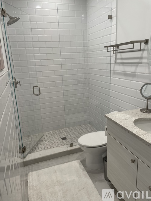 A white tiled bathroom with a toilet, sink, and shower.