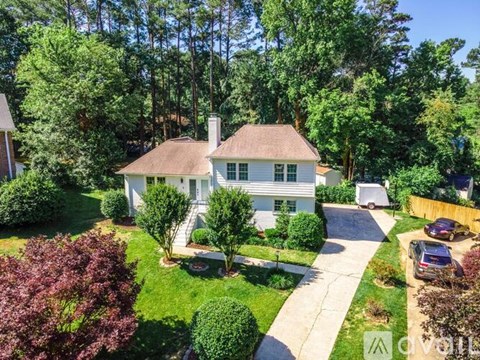 A white house with a brown roof is surrounded by greenery and trees.