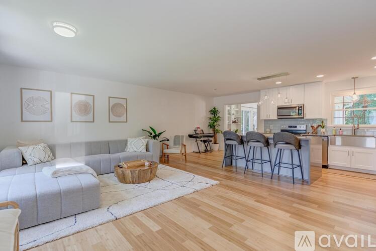A modern living room with a grey sofa, wooden floors, and a kitchen area in the background.