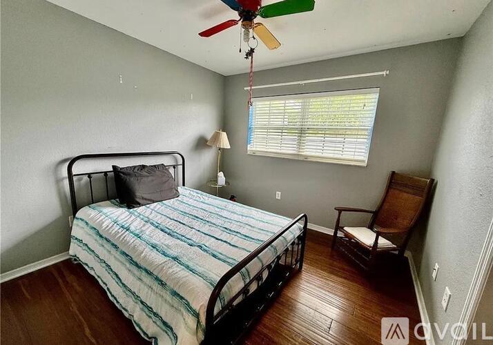 A bedroom with a bed, chair, and ceiling fan.