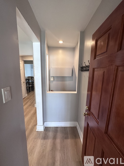 A hallway with a wooden door and a light switch on the wall.