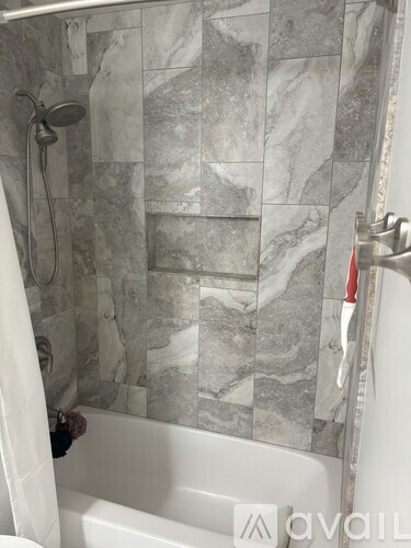 A bathroom with a marble tile wall and a white bathtub.