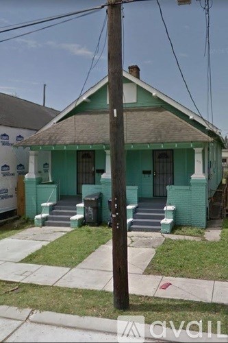 A green house with a porch and a brown telephone pole in front.