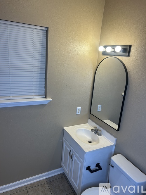 A bathroom with a sink, toilet, mirror, and window.