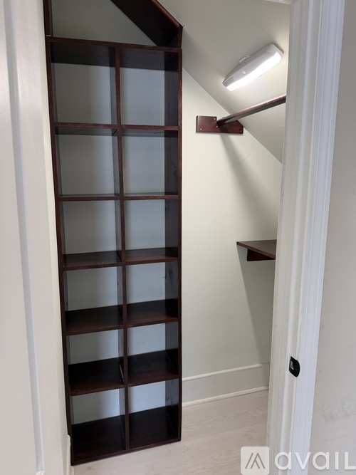 A tall, narrow shelving unit with brown shelves and a light on.