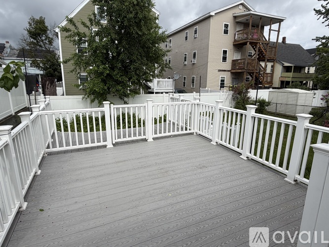 A wooden deck with white railings in front of apartment buildings.