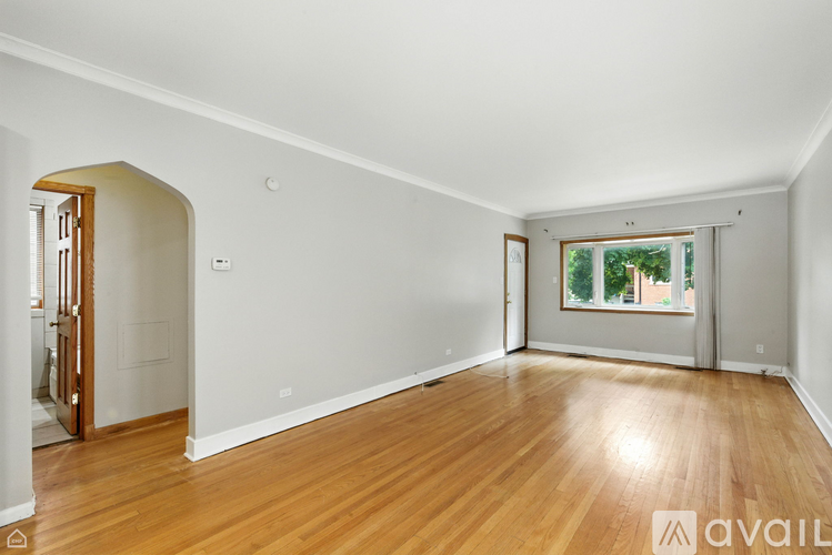 A room with wooden floors and white walls, with a window showing greenery outside.