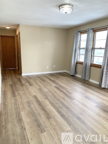 A room with wooden flooring and a window with curtains.