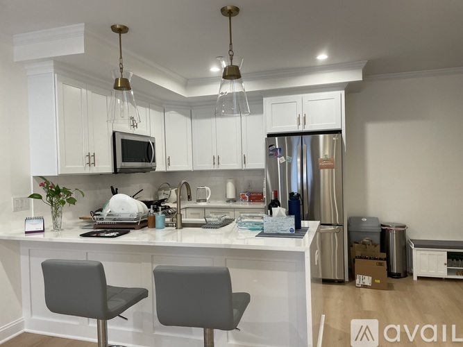 A kitchen with white cabinets and a white island with two grey chairs.