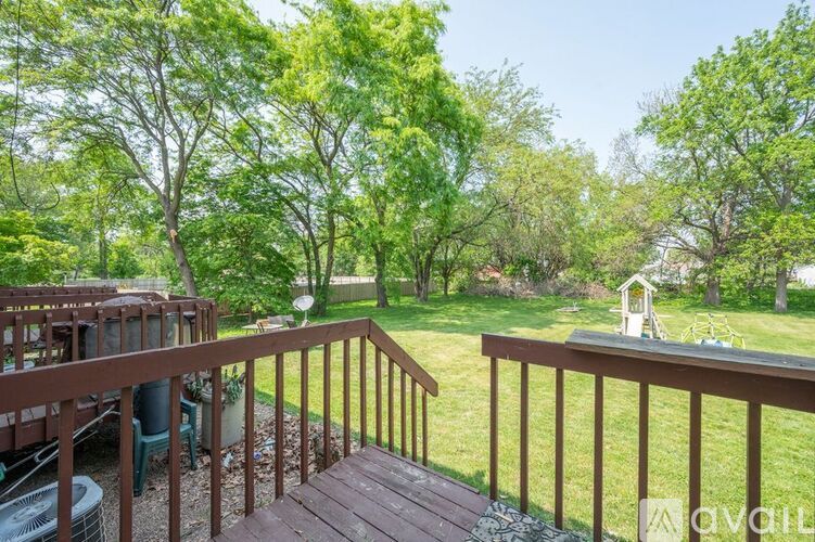 A deck with a railing overlooks a green lawn and trees.