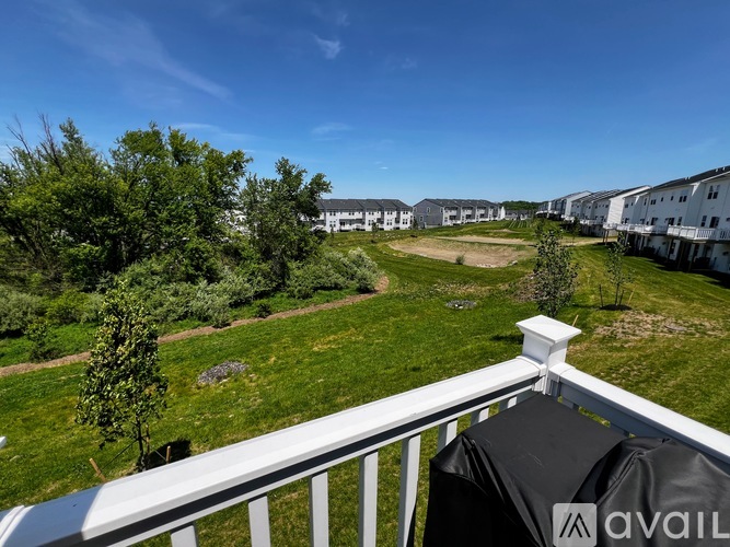 A balcony overlooks a grassy area with trees and apartment buildings in the distance.
