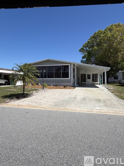 A modern building with a glass facade and a white roof is surrounded by a paved driveway and a few trees.