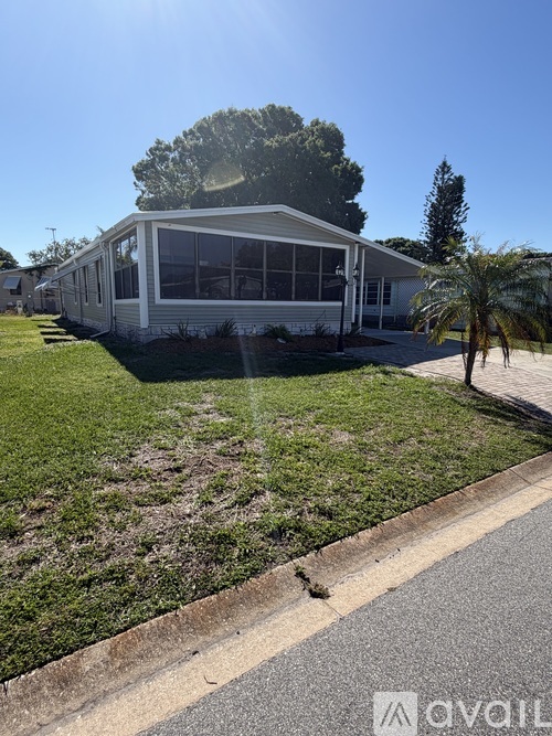 A house with a white exterior and a grey roof is surrounded by a grassy lawn and a sidewalk.