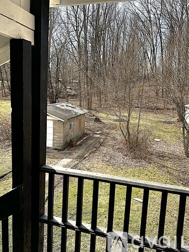 A view from a balcony looking out at a backyard with a small house and trees.
