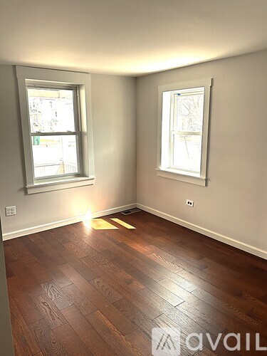 A room with wooden flooring and two windows.