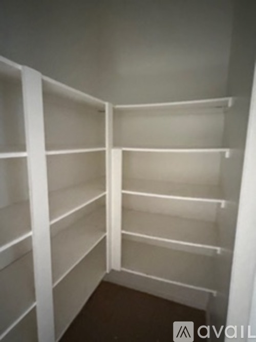 A white walk-in closet with shelves and a dark floor.