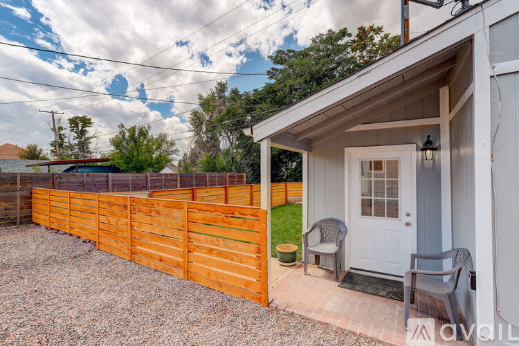 A small white house with a wooden fence and a gravel driveway.