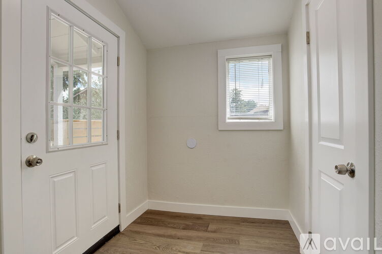 A small room with a door, a window, and a wooden floor.