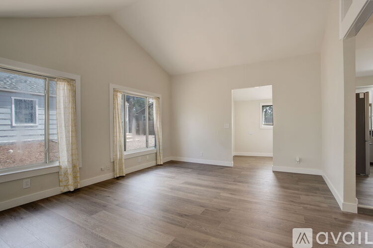 A spacious empty room with wooden flooring and two windows.