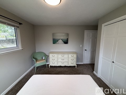 A bedroom with a white bed, green chair, and a white dresser with a mirror above it.