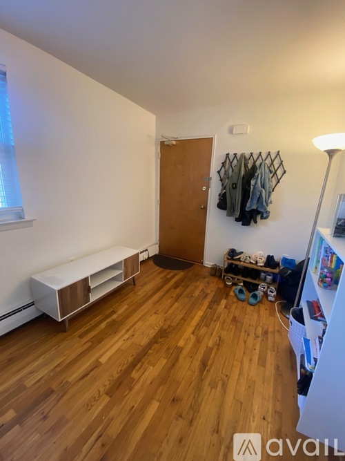 A room with wooden floors and a white wall with a coat hanger and a door.