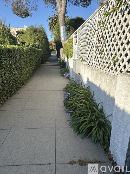 A sidewalk with a white fence and green plants on the side.