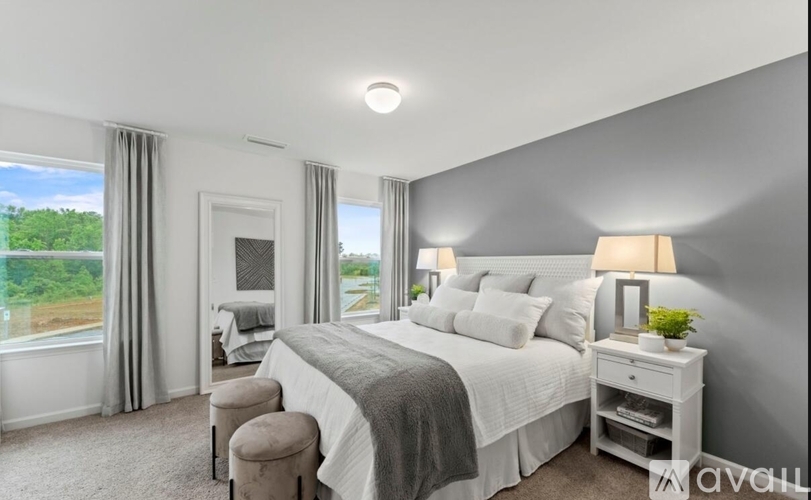 A well-lit bedroom with a large bed, a window with a view of trees, and a nightstand with a lamp.