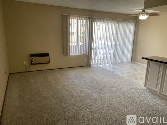 A room with a carpeted floor, a ceiling fan, and a window with blinds.