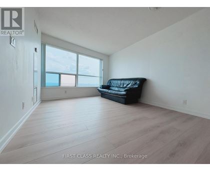 A black couch sits in a spacious room with a large window.