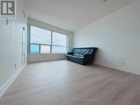 A black couch sits in a spacious room with a large window.