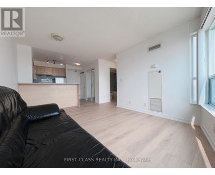 A black leather sofa sits in a spacious living room with hardwood floors and white walls.