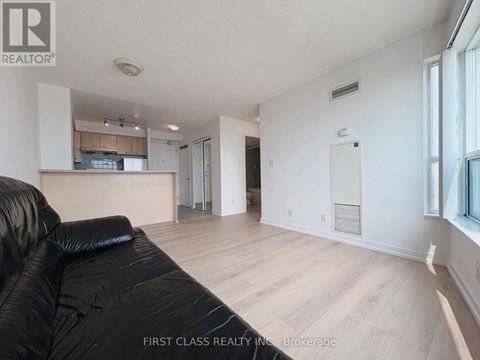 A black leather sofa sits in a spacious living room with hardwood floors and white walls.