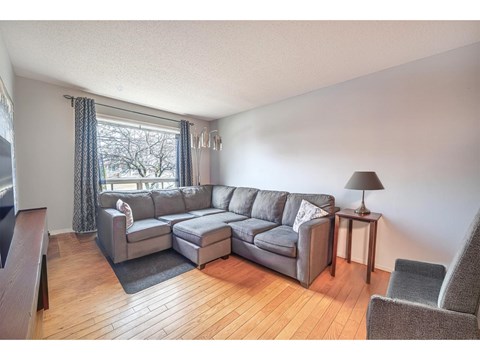 A grey sectional sofa with a chaise lounge and ottoman in a living room with a wooden floor and a window with curtains.