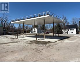 A large white carport with a metal roof is situated in a parking lot.