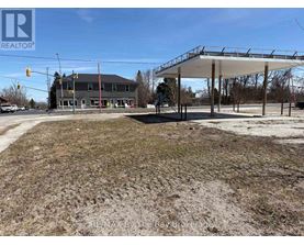 A large, empty field with a building and a carport in the background.