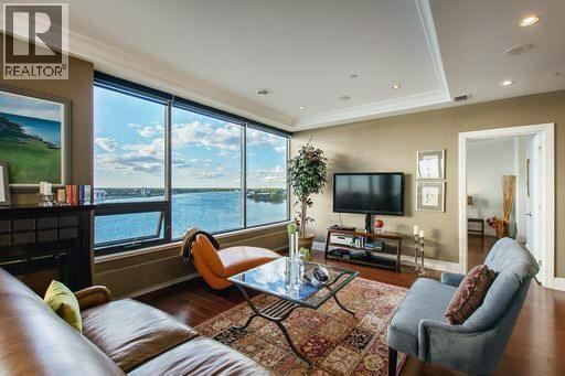 A living room with a brown leather couch, a glass coffee table, and a large window overlooking a body of water.