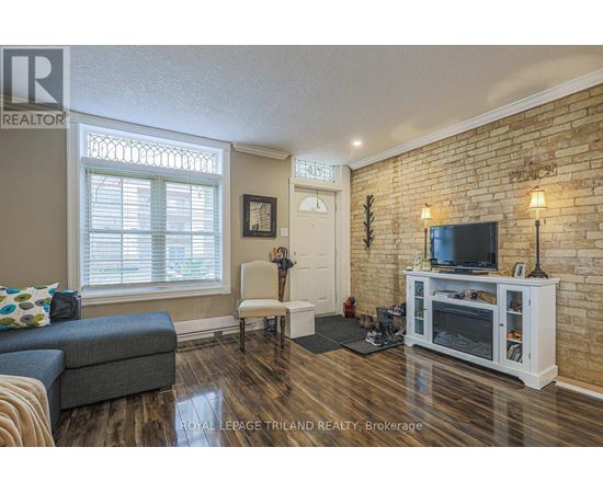A living room with a grey couch, a white chair, a television and a brick wall.