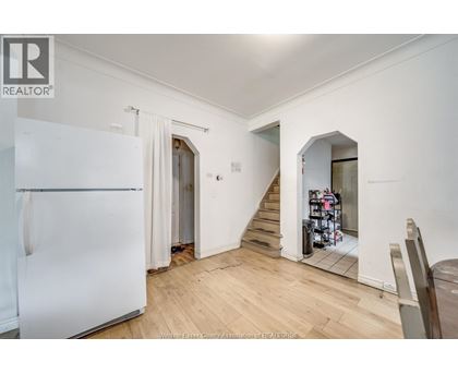A white refrigerator is in a kitchen with wood floors and white walls.