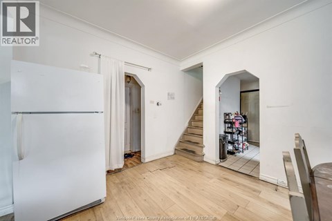 A white refrigerator is in a kitchen with wood floors and white walls.