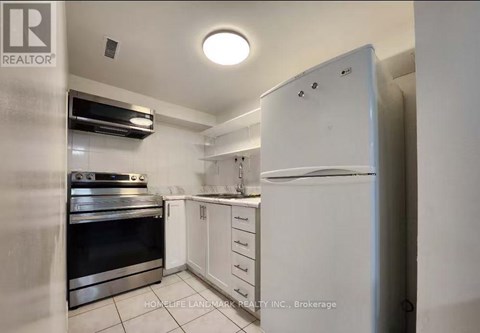 A white refrigerator stands in a kitchen with white cabinets and a black stove.