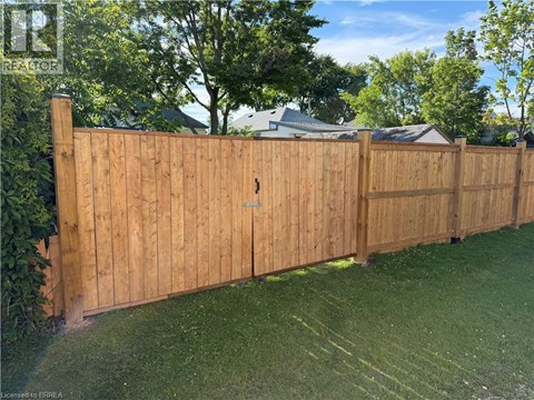 A wooden fence in a yard with a house and trees in the background.