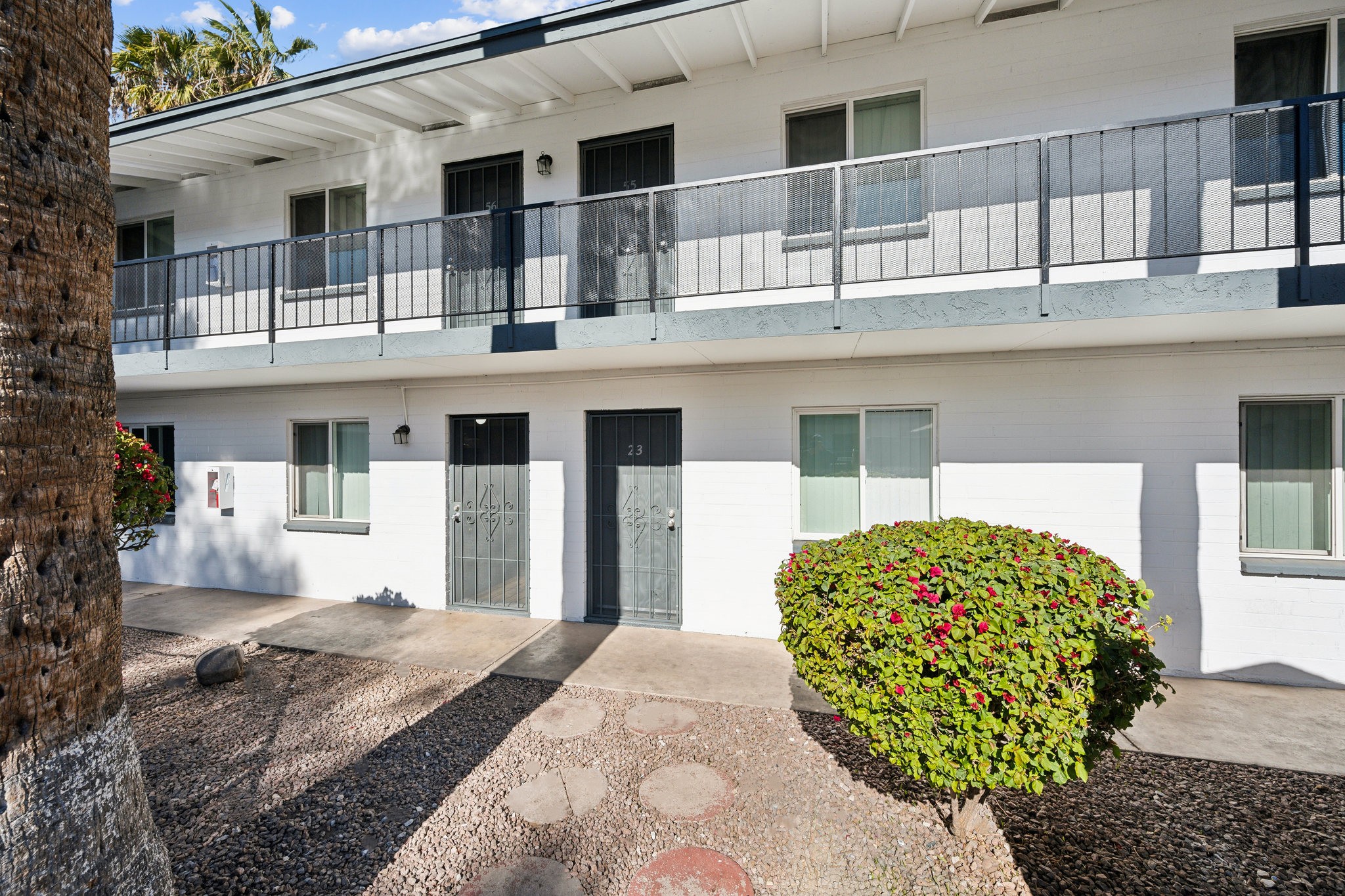 A white building with a balcony and a tree with red flowers in front.