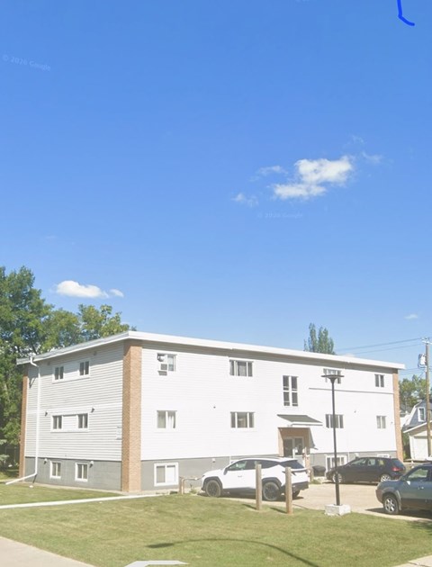 A large white building with a grey roof and a parking lot in front.