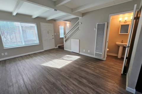 A room with wooden flooring and a staircase leading to another room.