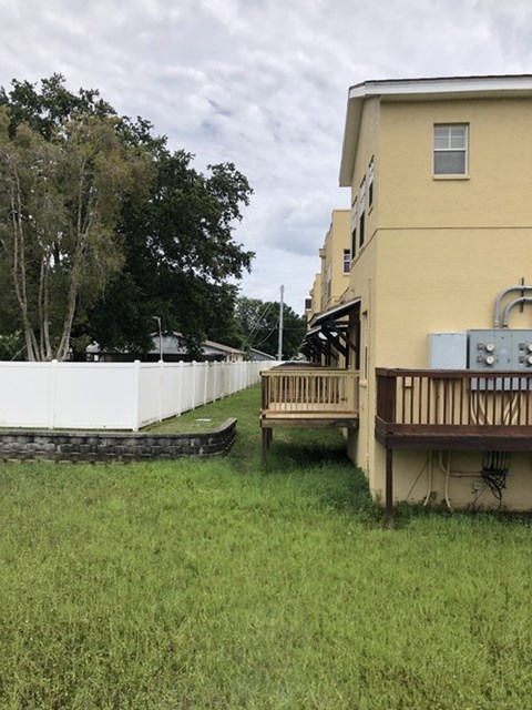 A yellow building with a white fence and a tree in the background.