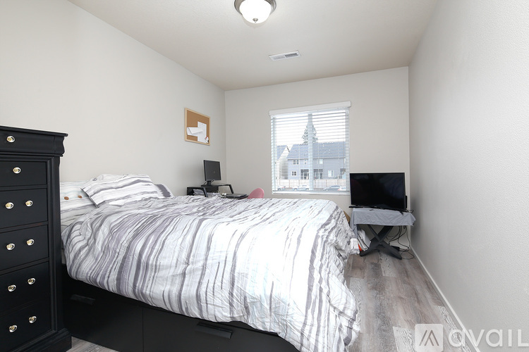 A bedroom with a bed, a dresser, and a window overlooking a building.